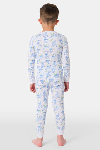A young boy stands barefoot, smiling and facing forward in Roller Rabbit's Kids Sleepy Sloth Pajamas—a white, long-sleeve cotton PJ set with playful blue and green sloth prints—against a plain white background.