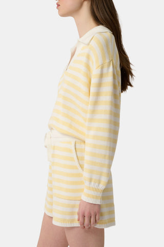 A person wears Roller Rabbit’s Striped Brie Short—a knit yellow and white horizontal striped short with a white drawstring at the elastic waistband and hands tucked in the front pockets.