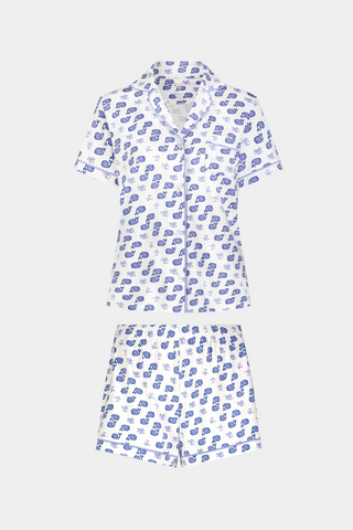 A woman with light brown hair and a gentle smile stands against a plain background, wearing Roller Rabbit's Moby Polo Pajamas—a women's short-sleeve sleepwear set featuring a whale print and crafted from soft Pima cotton.
