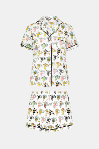 A smiling child in Roller Rabbit’s Kids Boo Crew Pajamas, crafted from soft Pima cotton, sits with arms raised on outdoor steps among women in coordinating patterned pajamas, all sharing a cheerful and relaxed moment together.