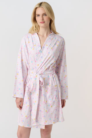 A woman with blonde hair models the Roller Rabbit Candy Heart Stripe Blake Robe—a light pink, knee-length Pima cotton robe with candy heart stripes and a waist tie—against a plain white background.