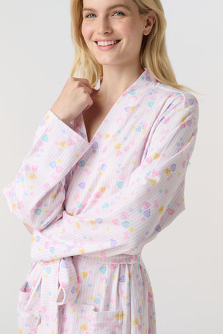 A woman with blonde hair models the Roller Rabbit Candy Heart Stripe Blake Robe—a light pink, knee-length Pima cotton robe with candy heart stripes and a waist tie—against a plain white background.