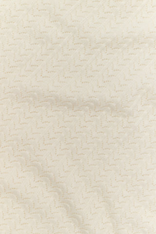 A woman wearing the Roller Rabbit Chain Pointelle Lauren Sweater in cream and white pants, standing against a white background.