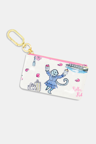The Roller Rabbit Georgetown Monkey Coin Pouch is a small cotton canvas pouch with a monkey in blue holding cupcakes, surrounded by suitcases, a boat, cherry blossoms, and "Roller Rabbit," finished with a gold keyring.