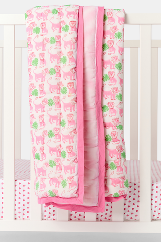 The Roller Rabbit Leo the Lion Baby Quilt features a soft cotton design with a pink border, white background, and playful pattern of pink elephants and green palm trees. A striped pink lining is visible along the folded edge.