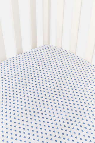 A white Hearts Crib Sheet by Roller Rabbit, featuring a repeating pattern of small, blue, hand-drawn heart shapes arranged in neat diagonal rows—an adorable choice for baby bedding.