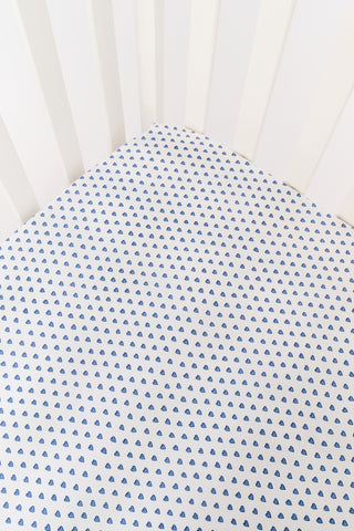 A white Hearts Crib Sheet by Roller Rabbit, featuring a repeating pattern of small, blue, hand-drawn heart shapes arranged in neat diagonal rows—an adorable choice for baby bedding.