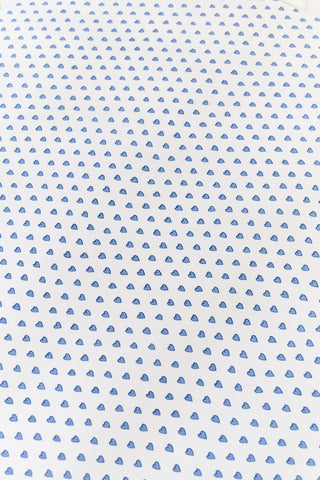 A white Hearts Crib Sheet by Roller Rabbit, featuring a repeating pattern of small, blue, hand-drawn heart shapes arranged in neat diagonal rows—an adorable choice for baby bedding.