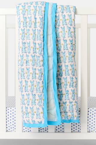 The Roller Rabbit Hoppy Baby Quilt features a playful blue and yellow Hoppy the Bunny pattern on white cotton, accented with a blue border and shown rolled up on a light surface.