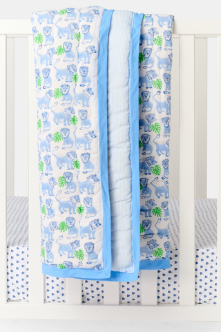 The Leo the Lion Baby Quilt by Roller Rabbit has a blue border, playful blue and white lions with green leaves on white, and a reverse side with light blue and white stripes.