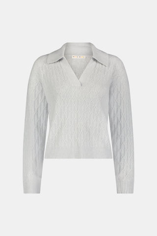 A woman wearing a light gray Cable Knots Rocio Sweater by Roller Rabbit, featuring a textured knit and V-neck, paired with matching knit pants, stands against a plain white background.
