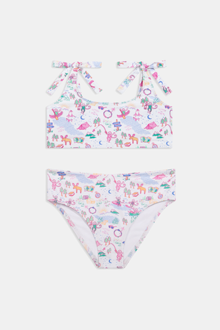 A girl wears the Roller Rabbit Kids Camp RR Cora Bikini, featuring a colorful pattern, adjustable tie straps, and high-waisted bottoms. She smiles against a white background, highlighting the comfort and UV protection of this swimwear.