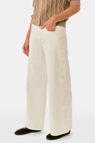 Wearing Roller Rabbit’s Elsa Eyelet Danielle Jean—a high-waisted, wide-leg style in ecru with delicate scalloped lace trim along the sides—paired with a white top and black Mary Jane shoes, the individual stands against a plain white background.