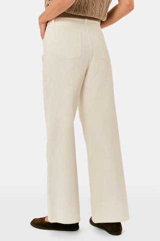 Wearing Roller Rabbit’s Elsa Eyelet Danielle Jean—a high-waisted, wide-leg style in ecru with delicate scalloped lace trim along the sides—paired with a white top and black Mary Jane shoes, the individual stands against a plain white background.