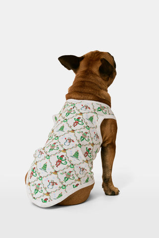 A woman wears a SERFLEX Deck The Halls Bailey Pajamas set featuring a short-sleeved top and shorts with a white background and a repeating Christmas-themed pattern of elves, snowmen, and evergreen trees.