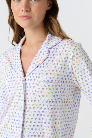 The Infant Disco Hearts Zipper Footie features white Pima cotton fabric with small, colorful, hand-drawn rainbow hearts evenly spaced across it. The soft material has a slightly wrinkled appearance.