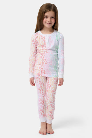 A girl with long brown hair stands barefoot, smiling and facing forward in Roller Rabbit Kids Monkey Juniper Pajamas—a matching set with a playful monkey print—against a plain white background.