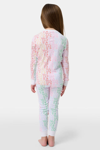 A girl with long brown hair stands barefoot, smiling and facing forward in Roller Rabbit Kids Monkey Juniper Pajamas—a matching set with a playful monkey print—against a plain white background.
