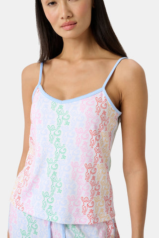 A woman stands barefoot wearing the Roller Rabbit Disco Monkey Lily Set, a matching Pima cotton pajama set featuring a pastel lace-like pattern, sleeveless camisole top, and drawstring pants with pockets.