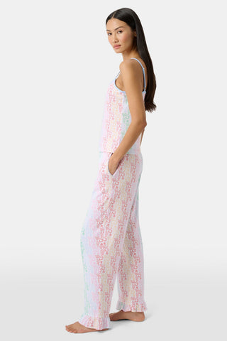 A woman stands barefoot wearing the Roller Rabbit Disco Monkey Lily Set, a matching Pima cotton pajama set featuring a pastel lace-like pattern, sleeveless camisole top, and drawstring pants with pockets.
