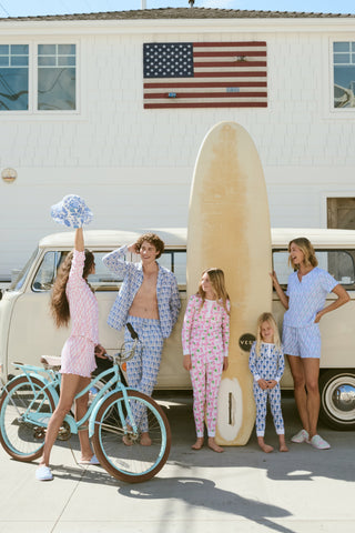 Family with surfboard and bicycles in front of a house with an American flag.