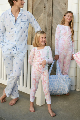 A girl with long brown hair stands barefoot, smiling and facing forward in Roller Rabbit Kids Monkey Juniper Pajamas—a matching set with a playful monkey print—against a plain white background.