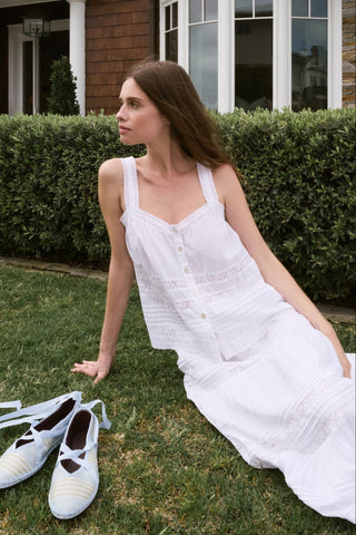Woman in a white dress sitting on grass next to a pair of white shoes.