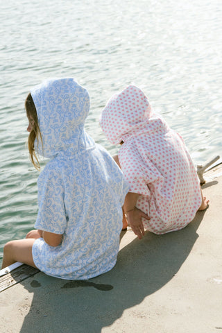 A young child smiles at the camera while wearing the Roller Rabbit Kids Monkey Jesse Cover Up, a light blue and white terry zip-up onesie with a playful animal pattern, against a plain background.