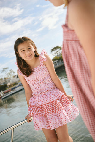 A young girl wears the Roller Rabbit Kids Starry Dot Tory Top in pastel pink with flutter sleeves, paired with a matching skirt featuring red stars and white polka dots. Only her torso and part of her face are visible.