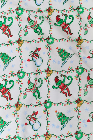 A woman wears a SERFLEX Deck The Halls Bailey Pajamas set featuring a short-sleeved top and shorts with a white background and a repeating Christmas-themed pattern of elves, snowmen, and evergreen trees.
