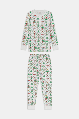 A child wearing SERFLEX Kids Deck The Halls Pajamas, featuring a repeating holiday pattern of snowmen, Christmas trees, and elves connected by garland on long-sleeved Pima cotton.