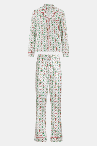 A woman wearing SERFLEX Deck The Halls Long Sleeve Polo Pajamas, a two-piece Pima cotton set featuring a repeating Christmas print of snowmen, elves, and trees on a white background with red piping.