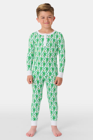 A young boy smiles at the camera, barefoot in Roller Rabbit’s Kids Monkey Pajamas— a matching top and bottom set featuring playful monkey prints and white cuffs, made from 100 pima cotton, against a plain white background.