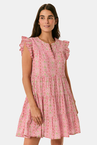 A woman models the Cora Floral Stripe Arles Top by Roller Rabbit—a loose, long-sleeved tunic in autumnal pink featuring a floral stripe block print and pintuck pleats on the chest—paired with white pants, against a plain light background.