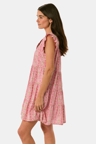 A woman models the Cora Floral Stripe Arles Top by Roller Rabbit—a loose, long-sleeved tunic in autumnal pink featuring a floral stripe block print and pintuck pleats on the chest—paired with white pants, against a plain light background.