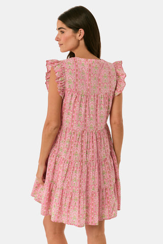 A woman models the Cora Floral Stripe Arles Top by Roller Rabbit—a loose, long-sleeved tunic in autumnal pink featuring a floral stripe block print and pintuck pleats on the chest—paired with white pants, against a plain light background.
