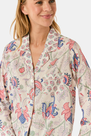 A woman stands against a plain white background, smiling slightly as she models the Amanda Leila Set from Roller Rabbit—a vintage-inspired cotton loungewear ensemble featuring a long-sleeve, button-up pajama top and matching shorts adorned with a colorful floral pattern.