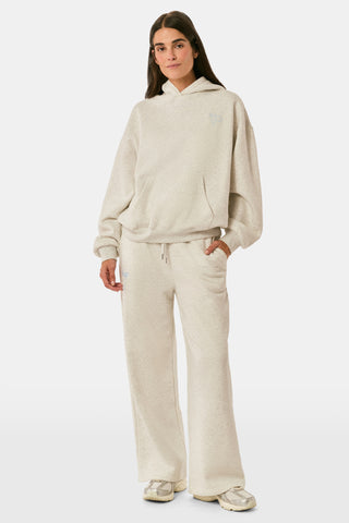A person is wearing the Roller Rabbit Sleep Club Mimi Sweatpants in light gray, featuring wide legs and crafted from velvety soft Dream Fleece with “Sleep Club” printed in light blue on the left thigh, paired with white sneakers and a cropped white top. The background is plain white.