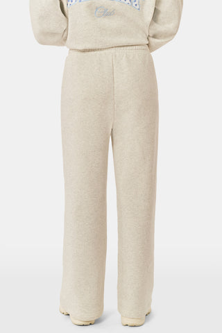 A person is wearing the Roller Rabbit Sleep Club Mimi Sweatpants in light gray, featuring wide legs and crafted from velvety soft Dream Fleece with “Sleep Club” printed in light blue on the left thigh, paired with white sneakers and a cropped white top. The background is plain white.