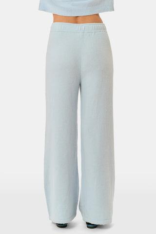 A woman poses with her arms crossed, wearing an icy blue AFFINA Moxie Cardigan with pearl-like buttons and matching drawstring pants.
