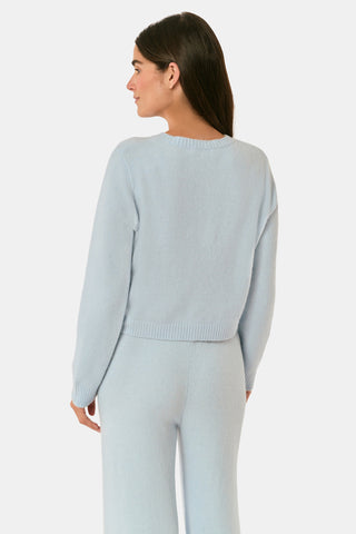 A woman poses with her arms crossed, wearing an icy blue AFFINA Moxie Cardigan with pearl-like buttons and matching drawstring pants.