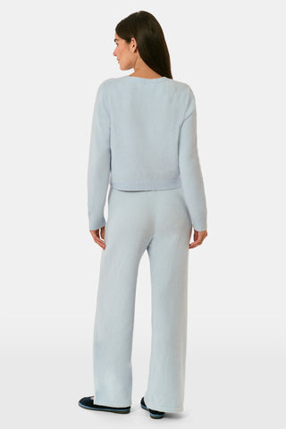 A woman poses with her arms crossed, wearing an icy blue AFFINA Moxie Cardigan with pearl-like buttons and matching drawstring pants.