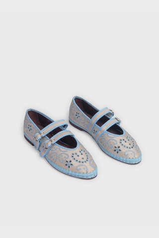 Person holding a pair of gray shoes with decorative elements, wearing a white dress with blue floral patterns.