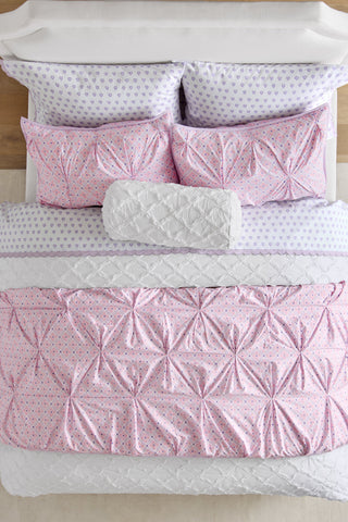 Pink and white quilted bedding set on a bed with wooden headboard