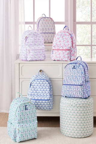 Collection of patterned backpacks on a dresser and stools in a bright room.