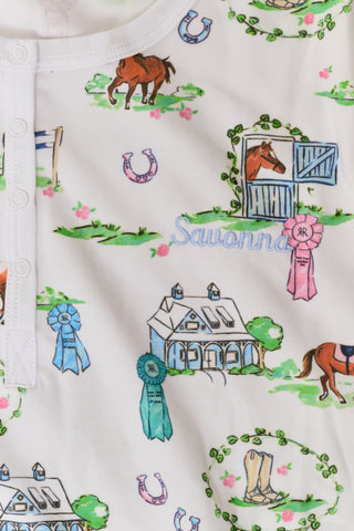 Meet the Saddle Up Pajamas by Roller Rabbit: a long-sleeved Pima cotton set on a white background, adorned with vibrant animal and tree motifs. The top features buttons at the neckline, while the elastic-waist pants offer comfy ease—ideal for horse girls who appreciate playful patterns and cozy comfort.