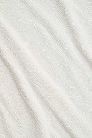 The Kids Hearts Pointelle Bridget Cami by Roller Rabbit is a white sleeveless camisole with thin straps and a small pink heart-shaped patch at the center of the chest. Crafted from soft pointelle cotton, it features a delicate scoopneck design. The background is light gray.