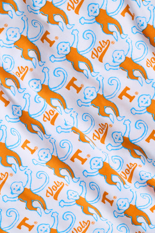 A woman stands barefoot against a plain white background wearing SERFLEX’s Tennessee Lovely Monkey Pajamas: a matching white women’s set with an all-over orange and brown monkey print, featuring long sleeves and full-length pants.