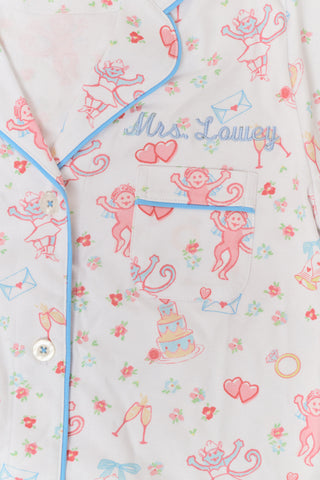 A woman smiles while wearing Roller Rabbit’s Monkey Said Yes Polo Pajamas—a short-sleeved, button-up top and matching shorts with a colorful, playful print featuring whimsical illustrations.