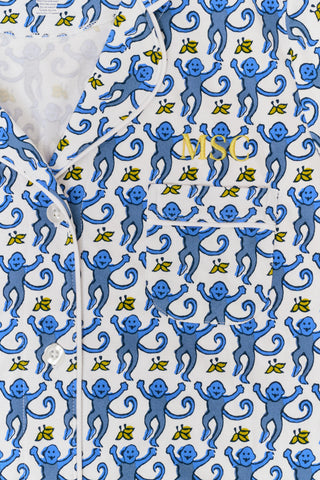 A woman with long blonde hair wears the Roller Rabbit Monkey Polo Pajamas, a matching pima cotton set with a blue and white floral and bird pattern, standing against a plain white background.